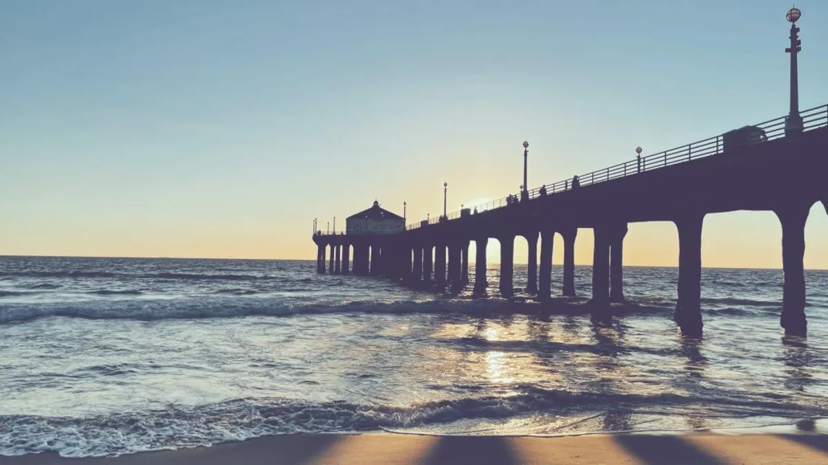 A South Bay pier silhouetted against a low sun, waves rolling in underneath.