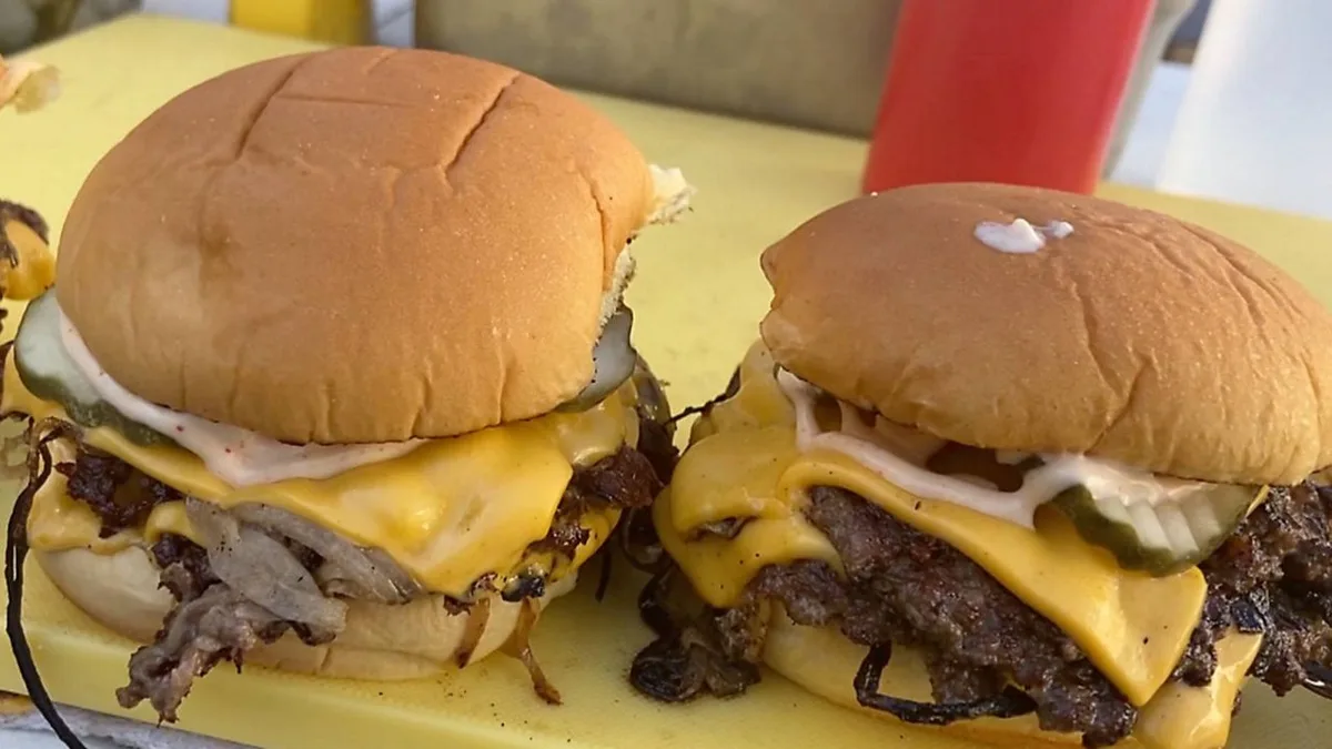 Two double cheeseburgers with grilled onions on a yellow board.